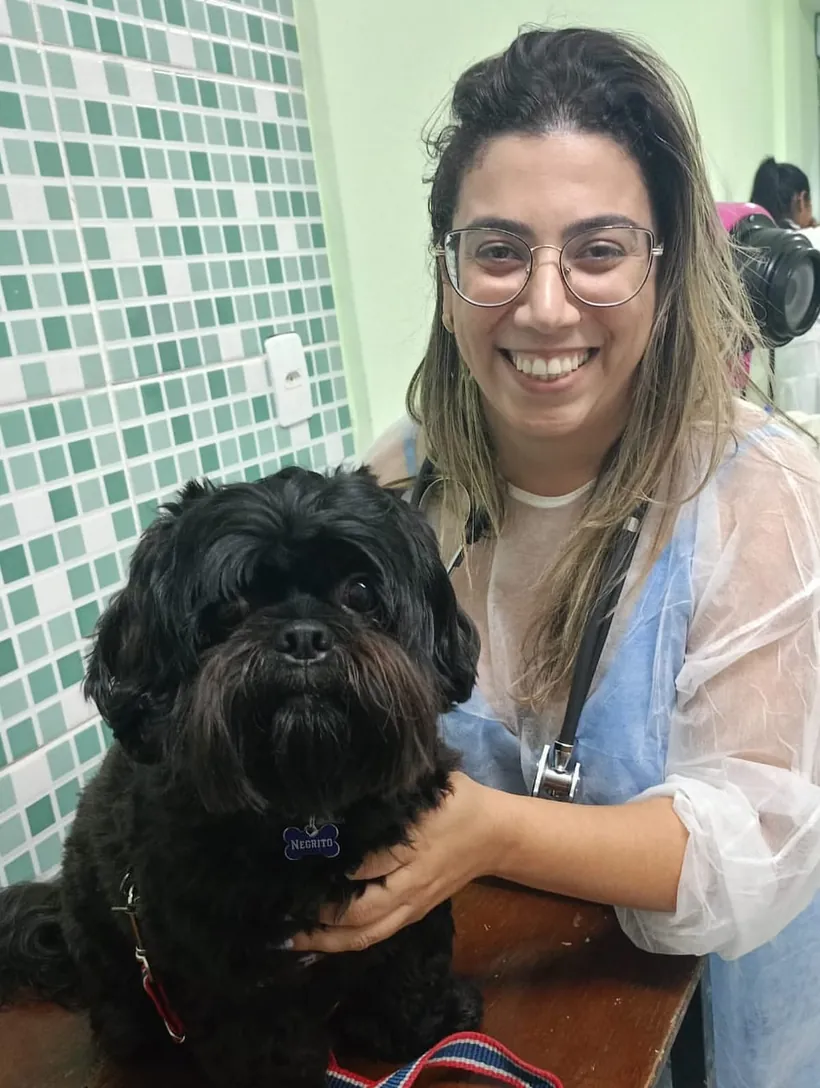 Sara, fundadora da Amoreco, sorrindo ao lado do Negrito, um cachorrinho preto e peludo